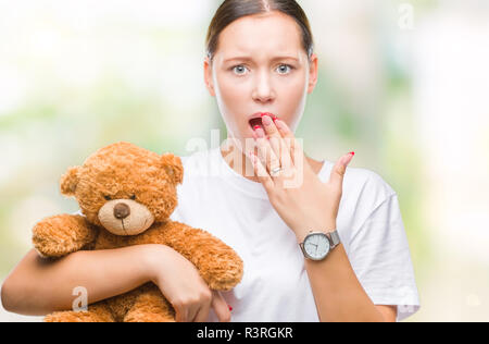 Young caucasian woman holding nounours plus couvrir la bouche avec fond isolé part choqué avec honte pour erreur, expression de la peur, peur de Banque D'Images