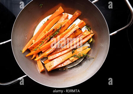 Les légumes racines, carottes glacées avec le thym, le gingembre et le miel dans une poêle de fer sur la cuisinière noire, high angle view from above Banque D'Images