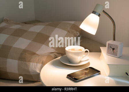 Table de chevet avec du café frais, réveil, téléphone et d'adresses, concept pour une bonne nuit de sommeil et un réveil reposé le matin Banque D'Images