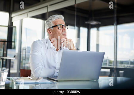 Businessman sitting in office, pensant Banque D'Images