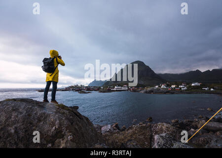 La Norvège, les îles Lofoten, vue arrière de l'homme debout sur un rocher à l'autre de prendre une photo Banque D'Images