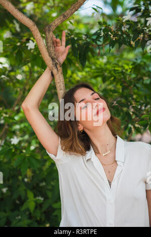 Jeune femme en serre, s'appuyant sur l'arbre avec les yeux fermés, portrait Banque D'Images