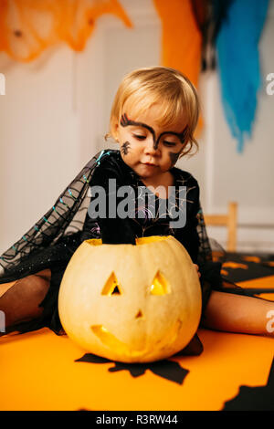 Portrait de petite fille avec visage peint et fancy dress sitting on table jouant avec Jack O'Lantern Banque D'Images