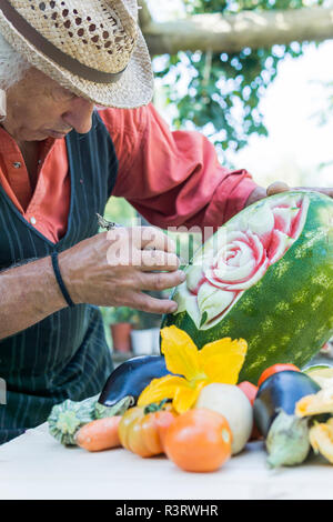 L'homme principal travaillant sur une pastèque avec outil de sculpture Banque D'Images