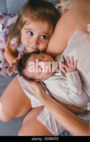 Mother holding her baby close avec sœur se sentir ses cheveux