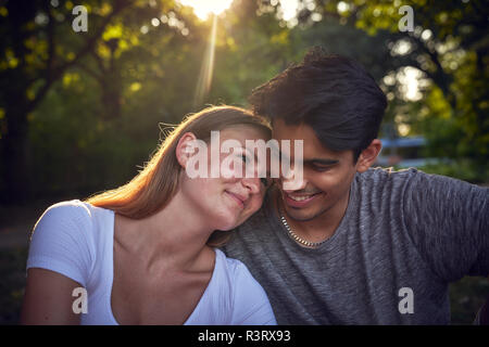 Couple assis dans un parc, profitant de coucher du soleil Banque D'Images