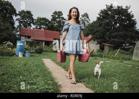 Femme heureuse avec Jack Russel terrier transportant des arrosoirs de jardin Banque D'Images