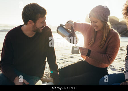 Smiling friends having coffee à la plage. Belle jeune femme servant du café dans une tasse pour l'homme à la mer. Banque D'Images