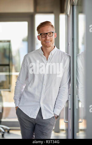 Portrait of smiling businessman in office leaning against window Banque D'Images