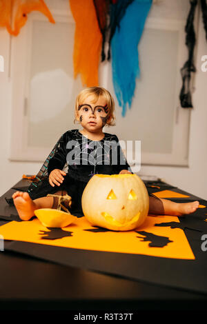 Portrait de petite fille avec visage peint et fancy dress sitting on table avec Jack O'Lantern Banque D'Images