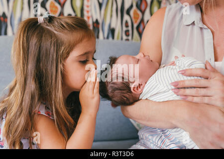 Mother holding her baby close avec sœur lui chuchotant à Banque D'Images