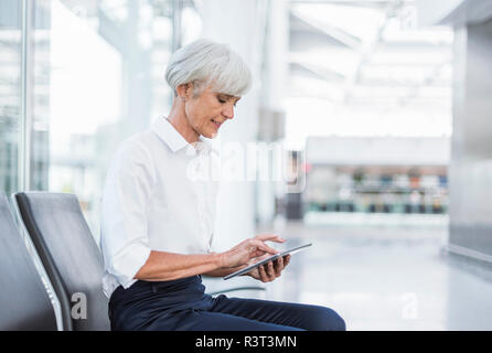 Senior businesswoman sitting in waiting area en utilisant tablet Banque D'Images