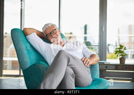 Portrait of smiling mature woman relaxing in fauteuil à la fenêtre à la maison Banque D'Images