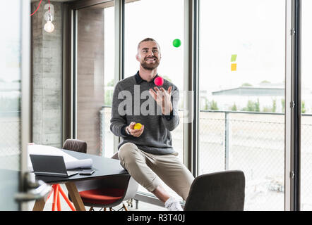 Smiling young businessman sitting at la fenêtre avec des boules de jonglage Banque D'Images
