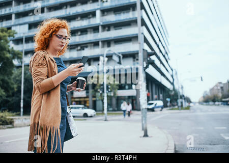 Jeune femme en attente de cross road, using smartphone Banque D'Images