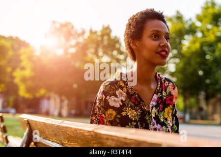 Jeune femme sur un banc dans un parc au coucher du soleil Banque D'Images