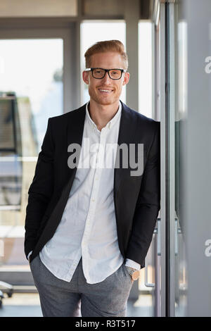 Portrait of smiling businessman in office leaning against window Banque D'Images