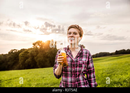 Smiling woman drinking beer in rural landscape Banque D'Images