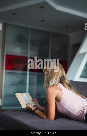 Jeune femme allongée sur un sofa reading a book Banque D'Images