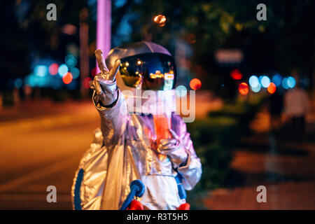 Spaceman dans la ville dans la nuit avec un verre à emporter la victoire de geste Banque D'Images