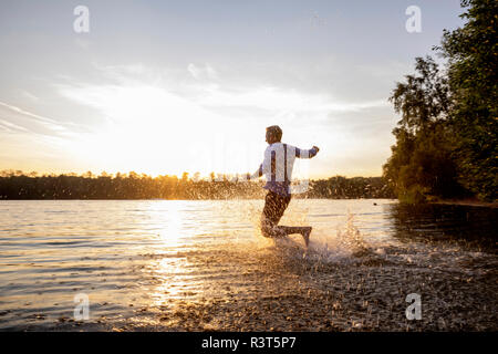Homme qui court dans le lac par le coucher du soleil Banque D'Images