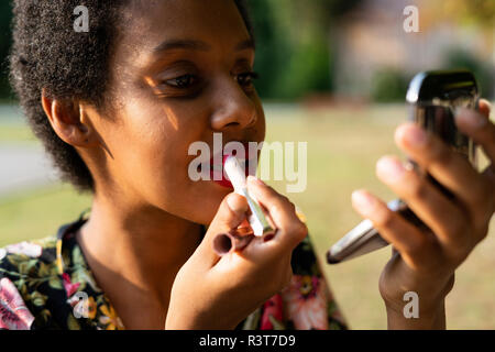 Portrait of young woman applying lipstick outdoors Banque D'Images