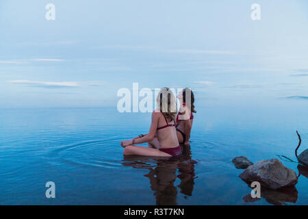 Deux jeunes femmes portant des bikinis, assis sur une pierre dans un lac Banque D'Images