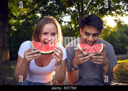 Young couple sitting in park, eating watermelon Banque D'Images