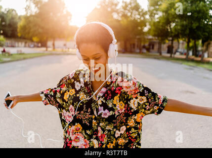 Happy woman with headphones dancing en plein air au coucher du soleil Banque D'Images
