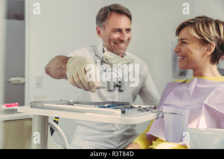 Dentiste mettre des instruments sur le bac après le traitement, regardant son patient smiling Banque D'Images