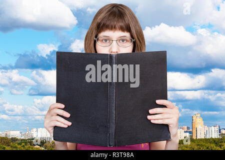 Lit fille gros livre bleu et nuages sur Ville Banque D'Images