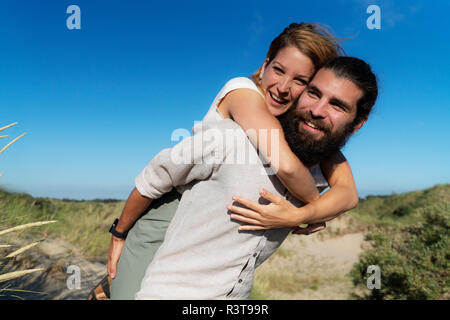 Young man carrying his girlfriend piggyback dans les dunes Banque D'Images