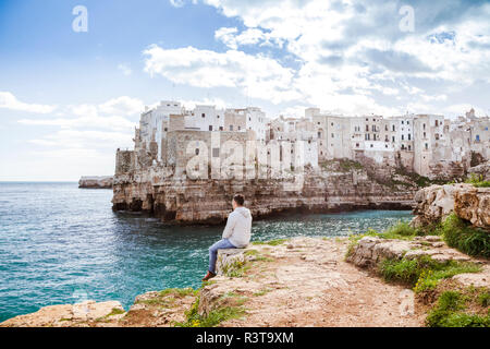 Italie, Pouilles, Polognano a Mare, vue de dos de l'homme sur des rochers à la détente à l'horizon Banque D'Images