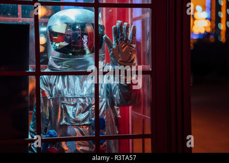 Spaceman debout dans une cabine téléphonique dans la nuit Banque D'Images