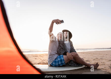 Couple camping sur la plage, en tenant vos autoportraits smartphone Banque D'Images