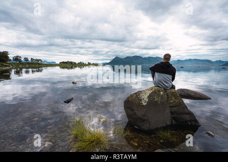 La Norvège, l'île de Senja, vue arrière de l'homme assis sur un rocher à la côte Banque D'Images