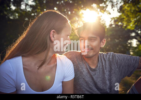 Couple assis dans un parc, profitant de coucher du soleil Banque D'Images