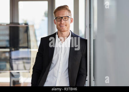 Portrait of smiling businessman in office leaning against window Banque D'Images