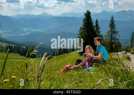 L'Allemagne, en Bavière, près de Brauneck Lenggries, happy young couple having a break assis dans le pré en paysage alpin Banque D'Images