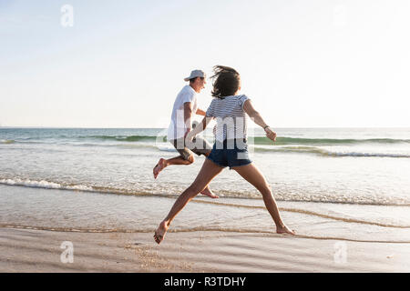 Jeune couple s'amusant sur la plage, courir et sauter à la mer Banque D'Images