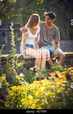 Young couple sitting on wall dans un parc, avec les bras autour de Banque D'Images