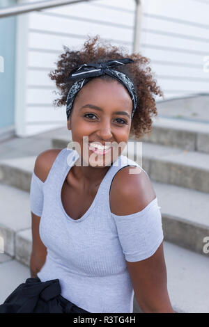 Portrait of happy young woman with hair-bande assis sur des escaliers Banque D'Images