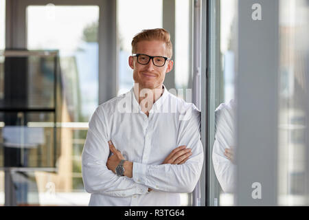 Portrait of smiling businessman in office leaning against window Banque D'Images