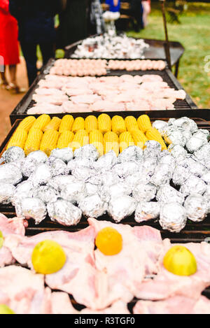 Les épis de maïs et de pommes de terre emballées dans du papier d'aluminium sur un barbecue. Banque D'Images