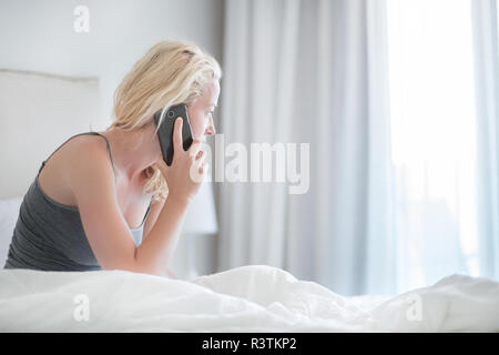 Femme parlant au téléphone le lit dans la matinée. Banque D'Images