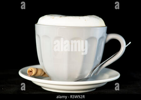 De délicieux cappuccino servi avec plaquette chocolat noisette isolées rouleaux fond noir Banque D'Images