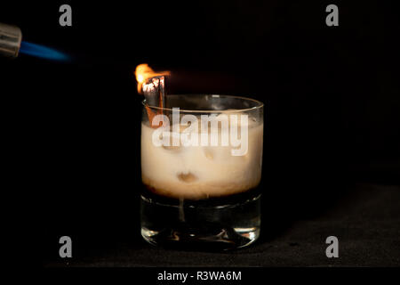 Cocktail avec de la cannelle en flammes, kahlua Baileys Irish Cream et sambuca avec fond noir isolé Banque D'Images