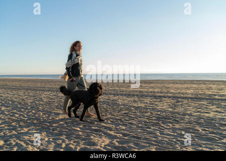 Jeune femme marchant sur la plage avec son chien Banque D'Images