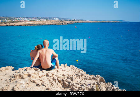 Couple assis ensemble sur un rocher près de l'eau transparente. Woman leaning sa tête sur l'épaule de l'homme. Concept d'amour, de soins, de tendresse, de voyage Banque D'Images