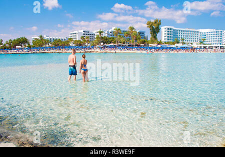 Blond caucasian man and woman avec le dos tourné, en maillot de bain, debout dans l'eau peu profonde, à la transparence, à la plage. Concept d'inspirati Banque D'Images